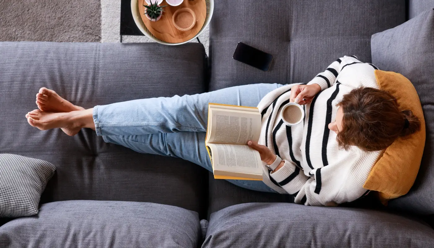 woman-comfortably-laying-on-couch-drinking-coffee-reading-a-book