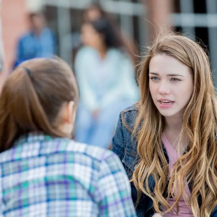 Two teenage girls talking outdoors near school building during serious conversation