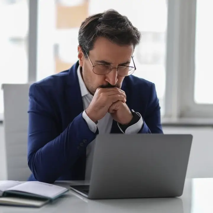 Man sitting at a desk looking thoughtful while working on his laptop.