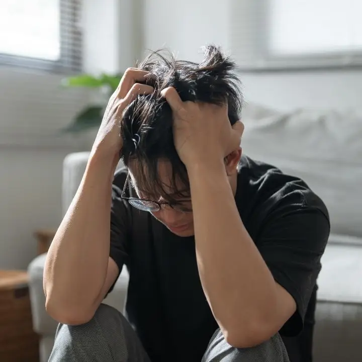 Adult person sitting on floor, holding head in visible distress