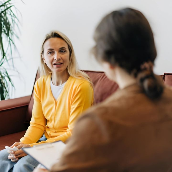 Woman sitting on a couch speaking with a therapist during a therapy session.
