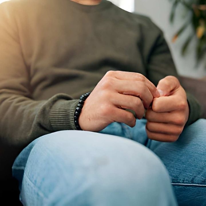 Close-up of a person sitting with hands clasped and fingers fidgeting on their lap during ERP Therapy.