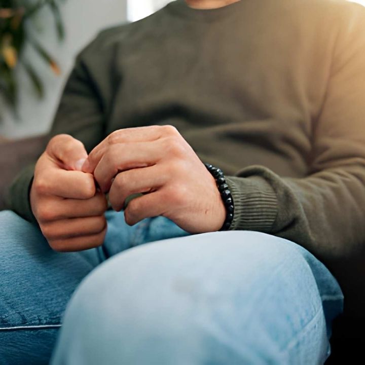 Close-up of a person sitting with hands clasped and fingers fidgeting on their lap during ERP Therapy.