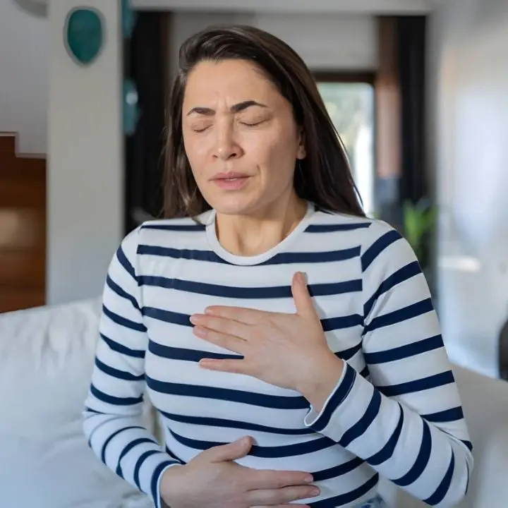 Woman with eyes closed holding her chest and abdomen, showing physical symptoms of anxiety.