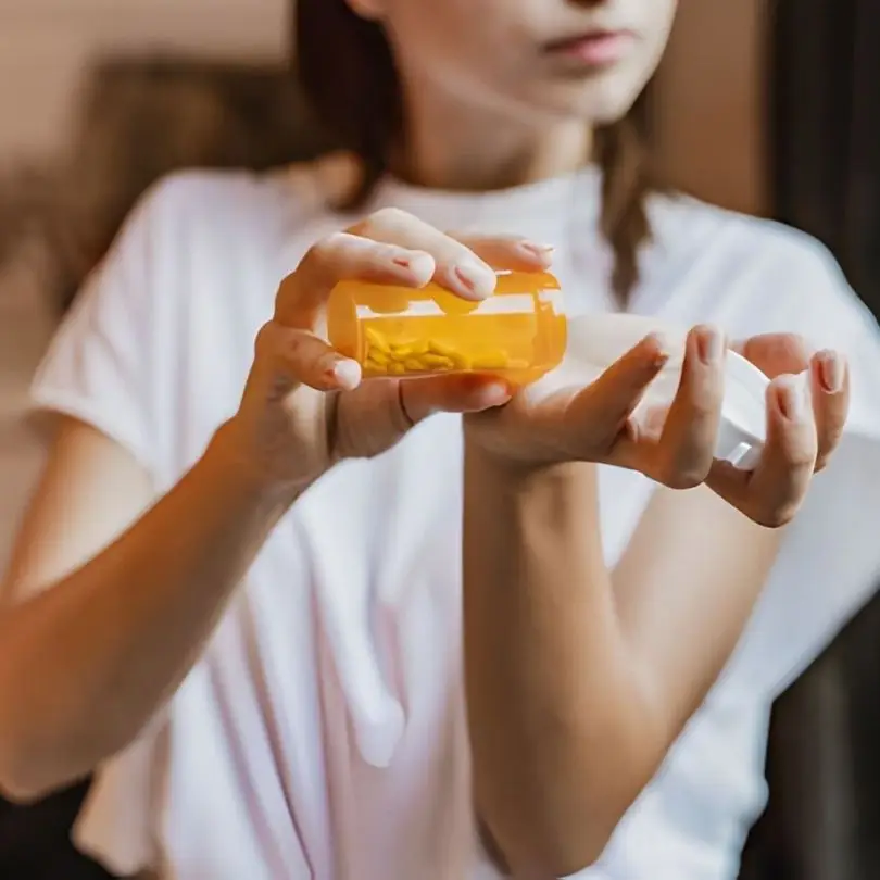 Woman pouring anxiety medication pills from a prescription bottle into her hand at home.