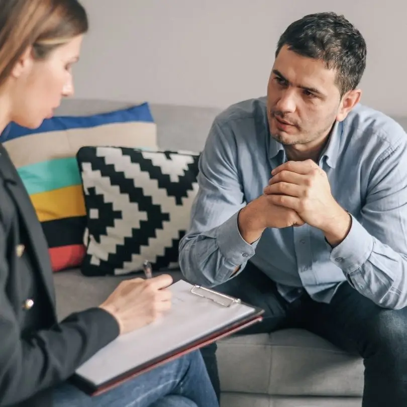 Therapist taking notes while speaking with a patient about anxiety treatment.