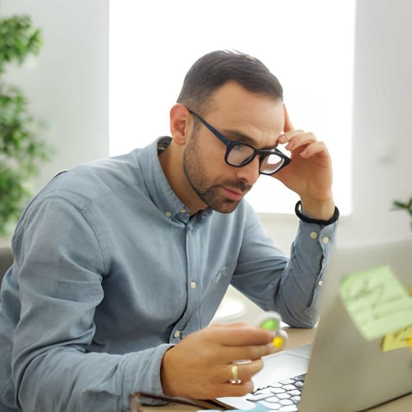 Man with OCD looking concerned while holding a fidget toy and working on a laptop.