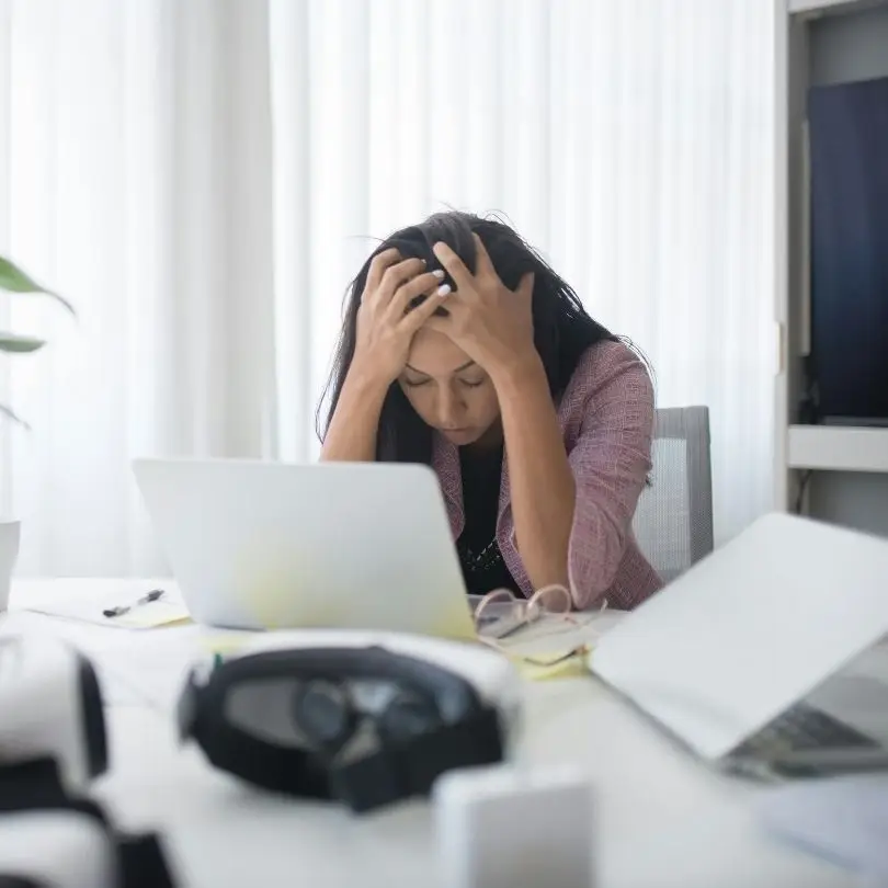 Woman holding her head while working on laptop at desk, experiencing a burnout.