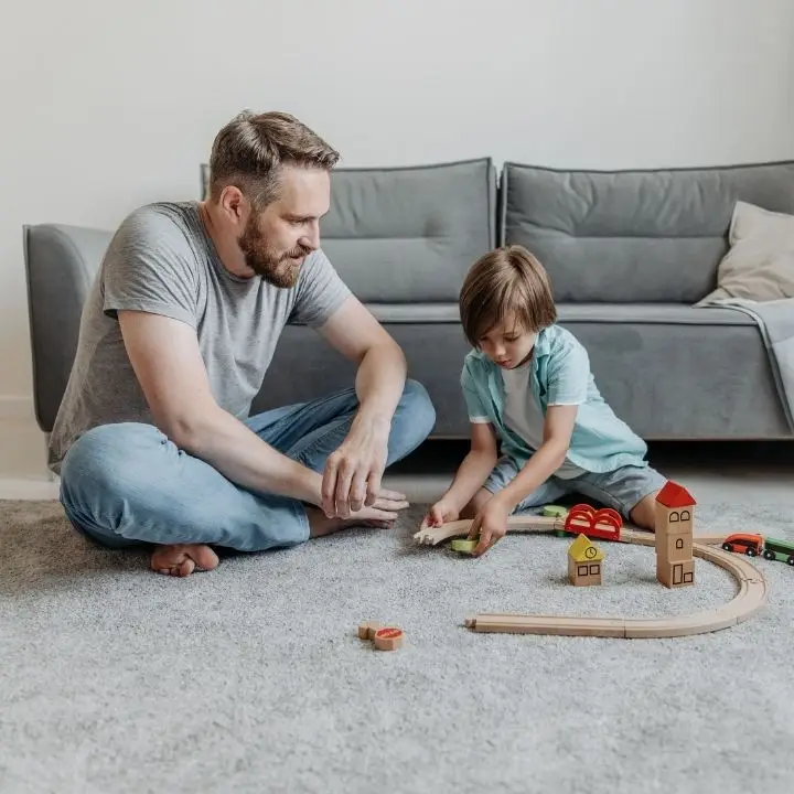 Father and child playing with wooden train set during family time.